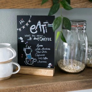 Schwarzer HMF Acryl Tischaufsteller Kreidetafel mit Holzfuß, beschriftet mit Kaffeemenü, auf Holzregal. Ideal für Gastronomie.
