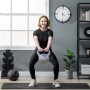 Frau macht Kniebeugen mit grauer 12 kg SPORTNOW Kettlebell mit blauem Griff. Perfekt für funktionales Gewichtstraining.