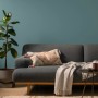 Wohnzimmer mit blaugrüner Alpina Wandfarbe, Couch und Zimmerpflanze.