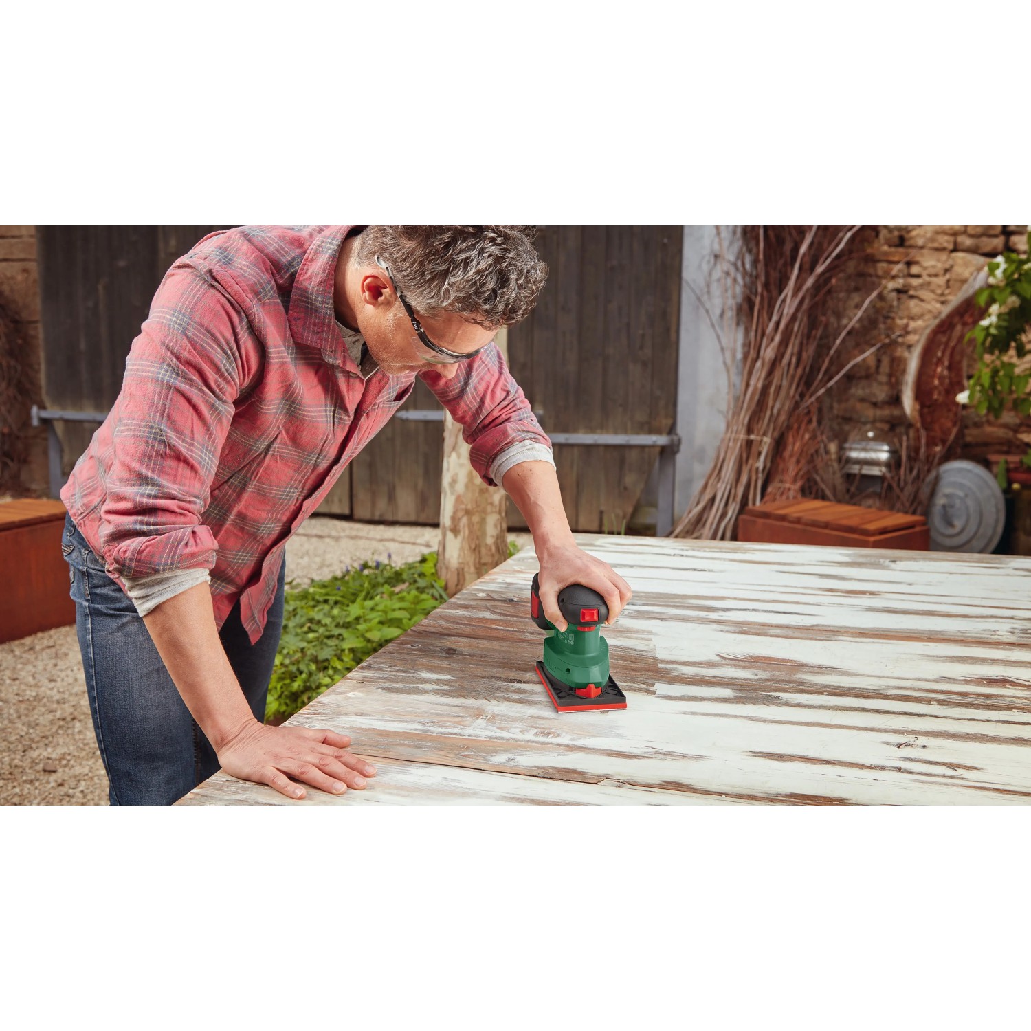 Mann schleift mit Bosch Akku-Multischleifer UniversalSander 18V-10 eine Holzplatte. Grüner Deltaschleifer für vielseitige Schleifarbeiten.