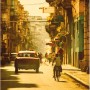 Komar Wandbild Cuba Streets: Gasse mit Oldtimer-Taxi und Radfahrer in warmen Farben.