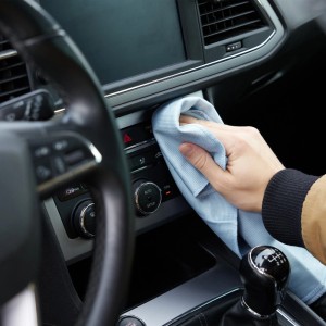 Hand reinigt mit blauem Mikrofasertuch das Armaturenbrett eines Autos.