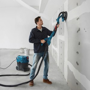 Mann schleift Wand mit Bosch Trockenbauschleifer GTR 55-225, Sauger im Hintergrund.