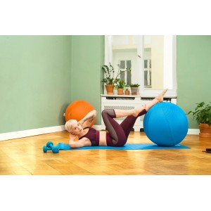 Frau macht Übungen mit blauem Sitting Ball Hocker (Petrol) auf einer blauen Matte.