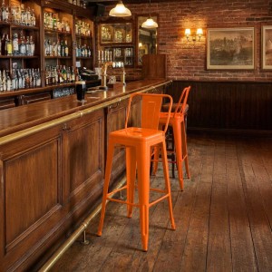 Zwei orangefarbene CLP Mason Barhocker aus Metall im Industrial-Stil an einer Holzbar. Ideal für Küche oder Bar.