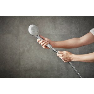 Hansgrohe Crometta 85 Vario Handbrause in Chrom, gehalten in Händen vor grauer Wand.