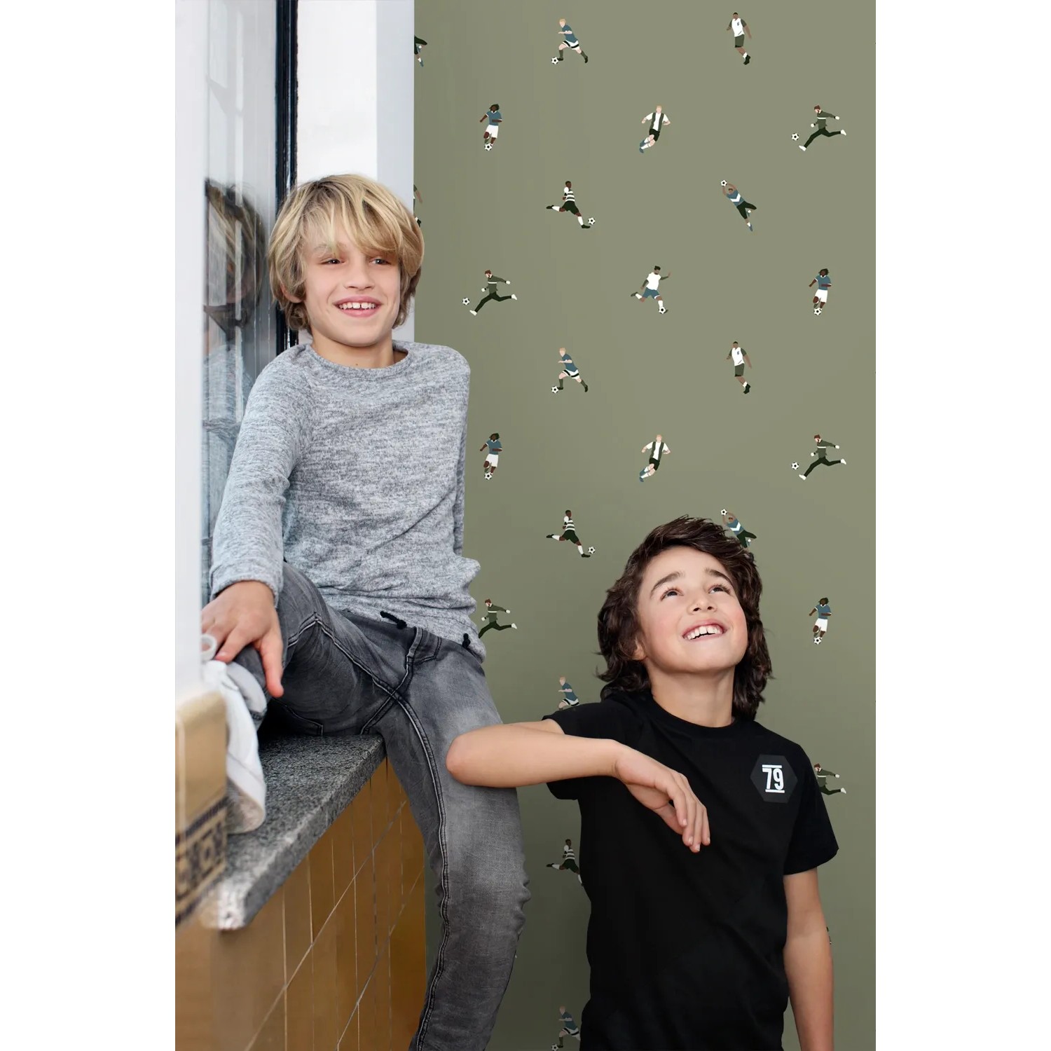 Olivgrüne Vliestapete mit Fußballspielern im Kinderzimmer, zwei Jungen lächeln. Dekorative Tapete.