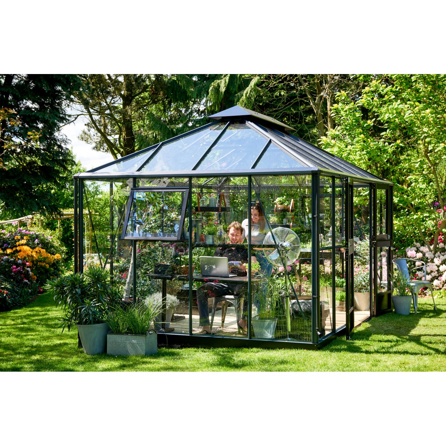 Juliana Gewächshaus Grand Oase 13, anthrazit, mit Personen, Pflanzen und Gartenzubehör.