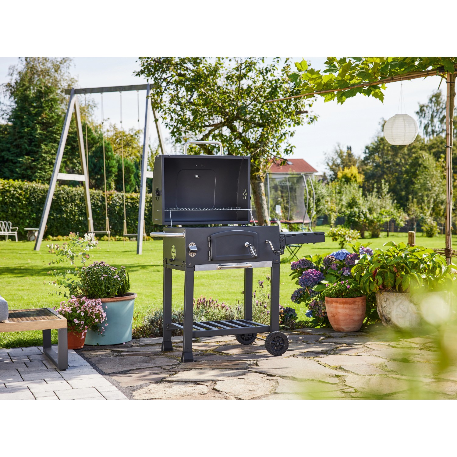 Jamestown Holzkohlegrillwagen Jaxon im Garten mit geöffnetem Deckel und Ablageflächen.