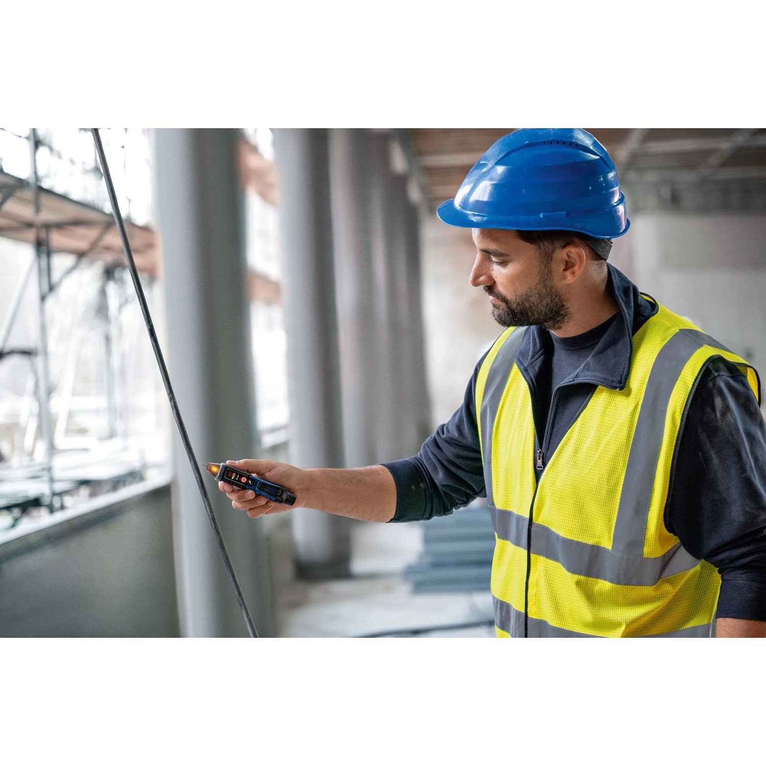 Mann prüft mit dem Bosch Professional GVD 1000-17 Spannungsprüfer eine Leitung auf einer Baustelle.