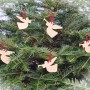 Fünf filigrane Deko Engel aus hellem Zirbenholz mit roter Schnur hängen als Christbaumschmuck an grünen Tannenzweigen.