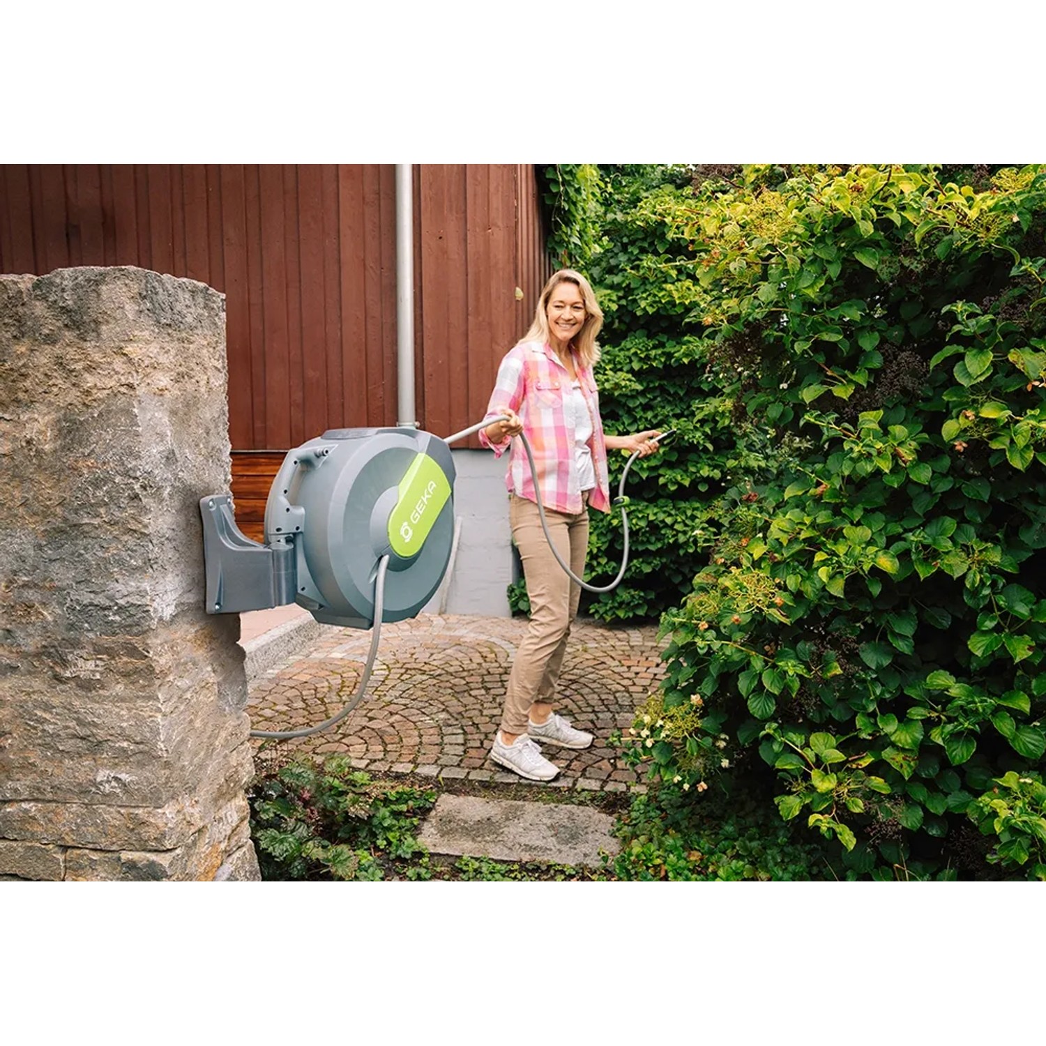 Graue Geka Schlauchbox K25 am Haus mit Frau beim Gießen im Garten.
