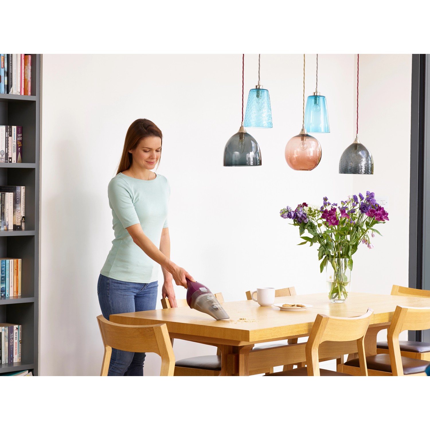 Frau reinigt Tisch mit Black+Decker Akku-Handstaubsauger NVC115W.